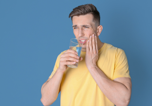 Brunette man portraying tooth sensitivity to cold while drinking water